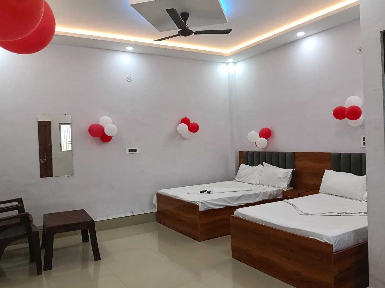 A hotel room with two beds, a ceiling fan, and red and white balloons.