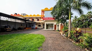 A hotel with a covered parking area, a grassy lawn, and a well-maintained garden with palm trees. - Hotel O EMERGE HOTELS (Chitrakoot)