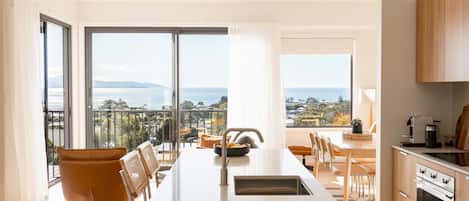 A modern kitchen with a central island, large windows, and a view of the sea.