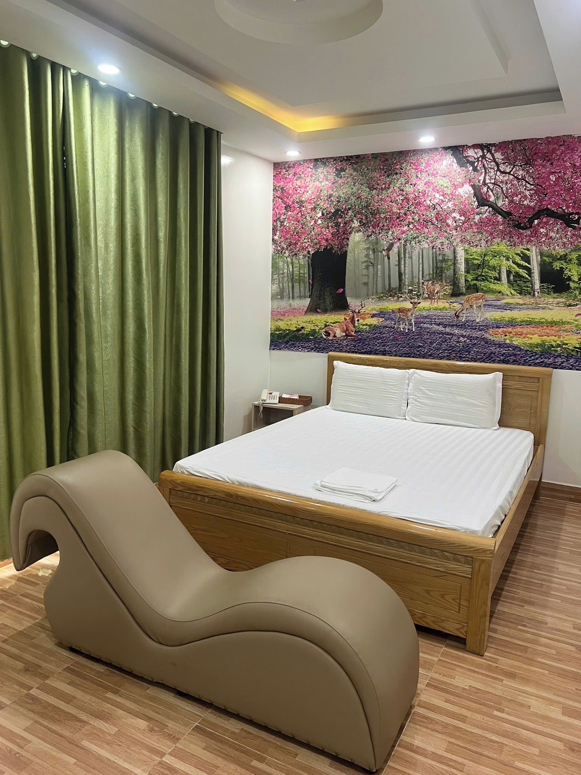 Habitación de hotel con cama, sofá curvo, mesita de noche con teléfono y un gran mural floral en la pared.