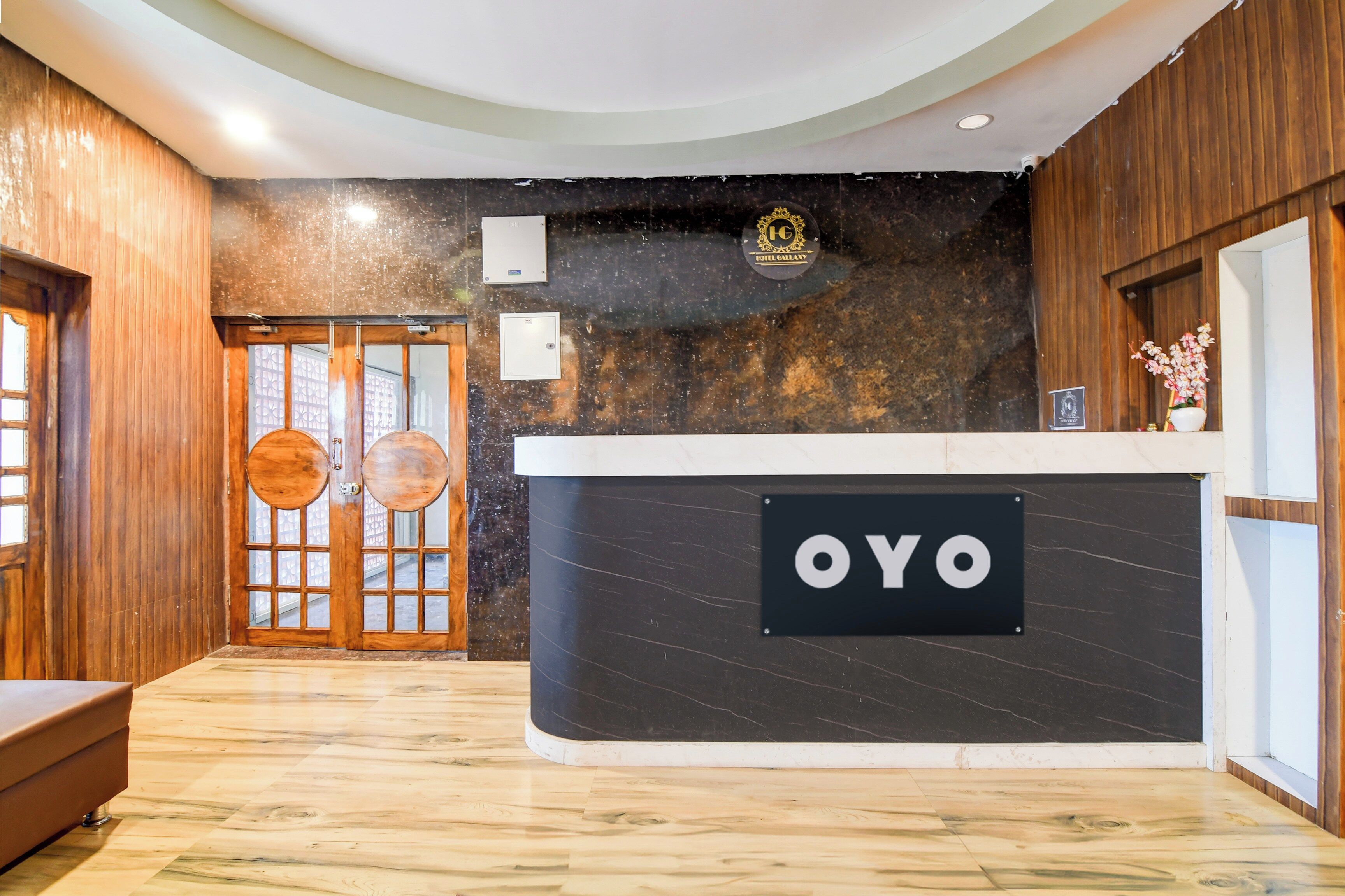 Un mostrador de recepción con un letrero que dice 'OYO' en el vestíbulo de un hotel con paneles de madera y suelo de mármol.