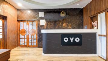Un mostrador de recepción con un letrero que dice 'OYO' en el vestíbulo de un hotel con paneles de madera y suelo de mármol.