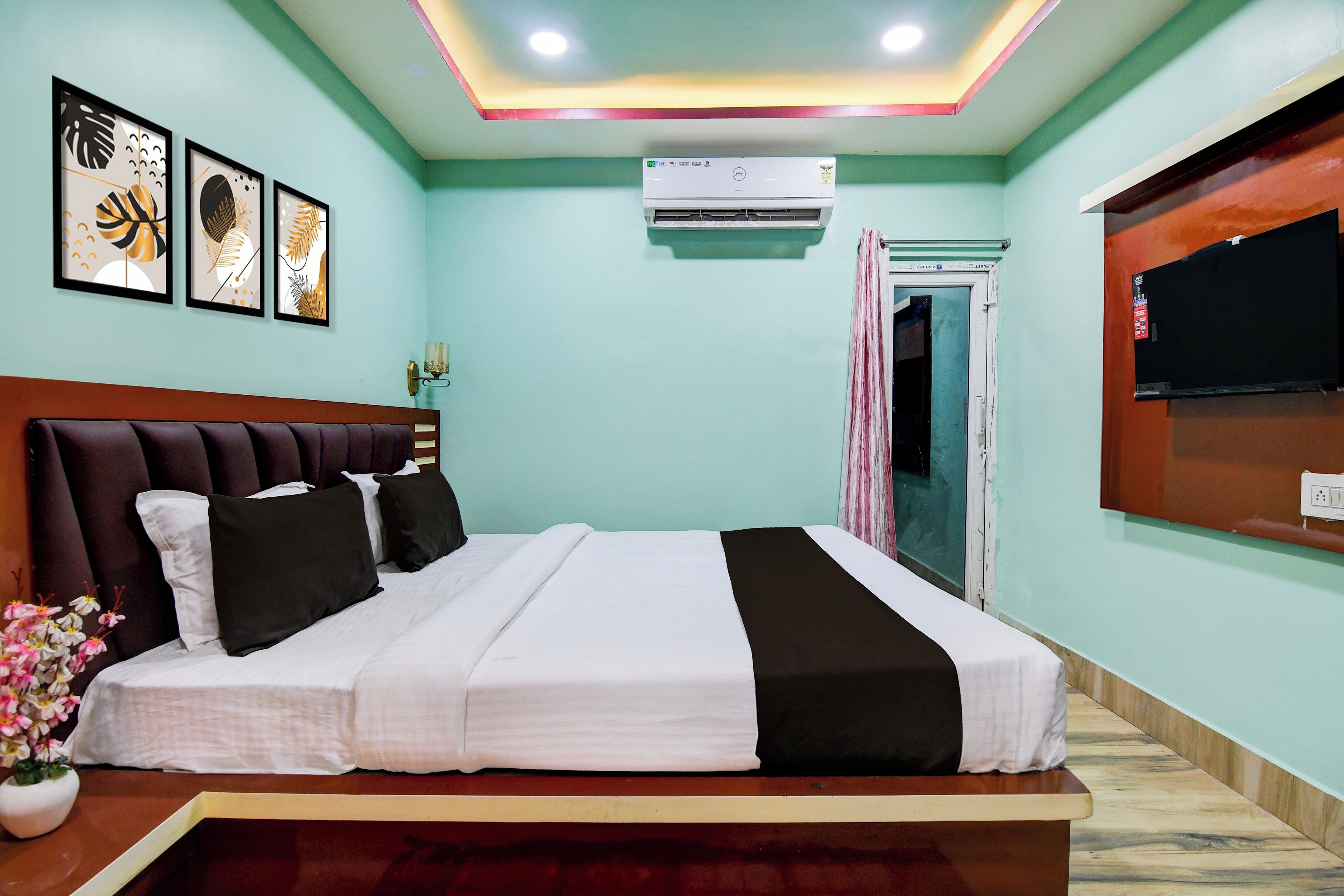 A hotel room with a bed, a flat-screen TV, an air conditioning unit, and framed artwork on the wall.