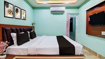 A hotel room with a bed, a flat-screen TV, an air conditioning unit, and framed artwork on the wall.