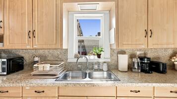 A kitchen with wooden cabinets, a double sink, a microwave, a coffee maker, and a window with a view of the sky.