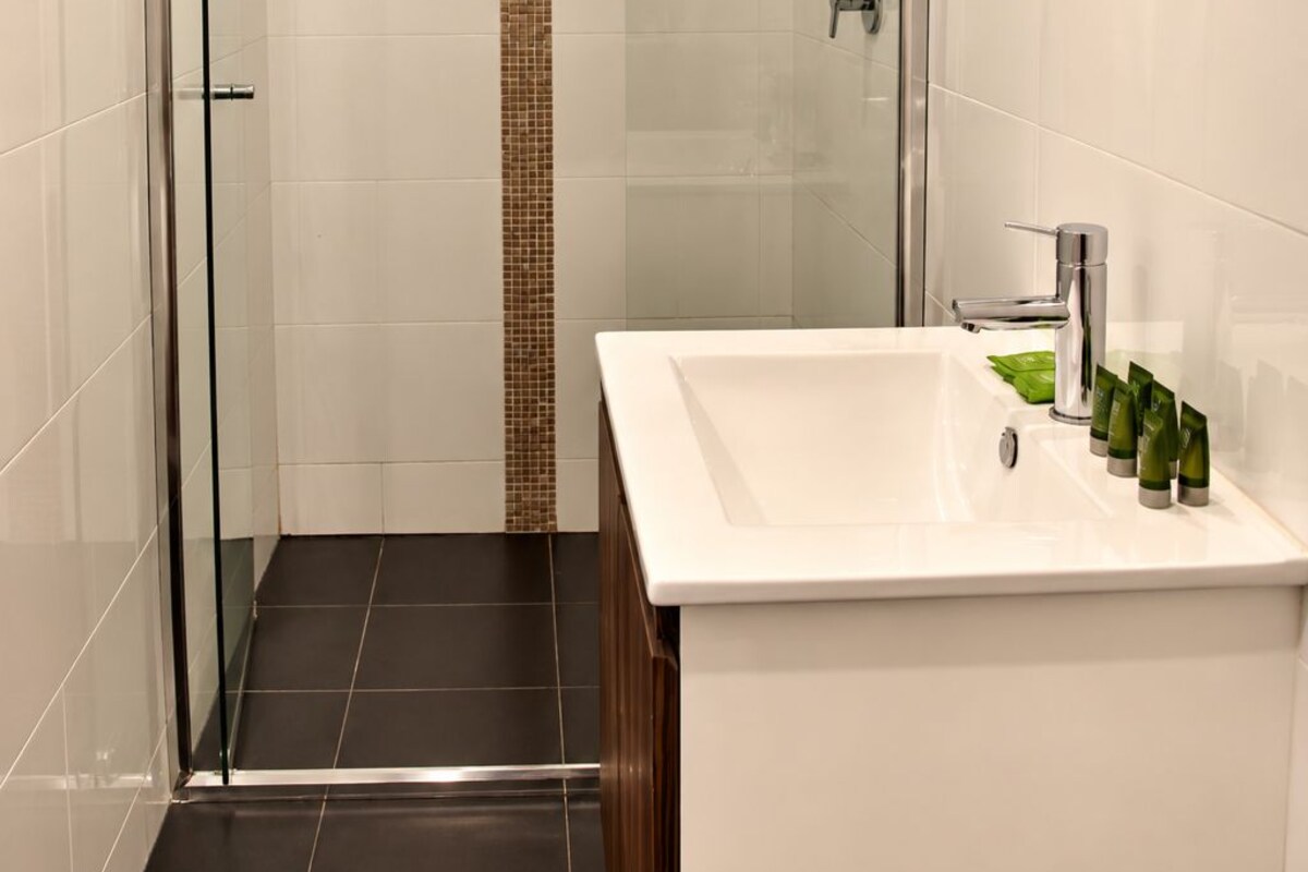 Une salle de bain moderne avec une douche à parois de verre, un lavabo blanc agrémenté d’articles de toilette et un miroir.
