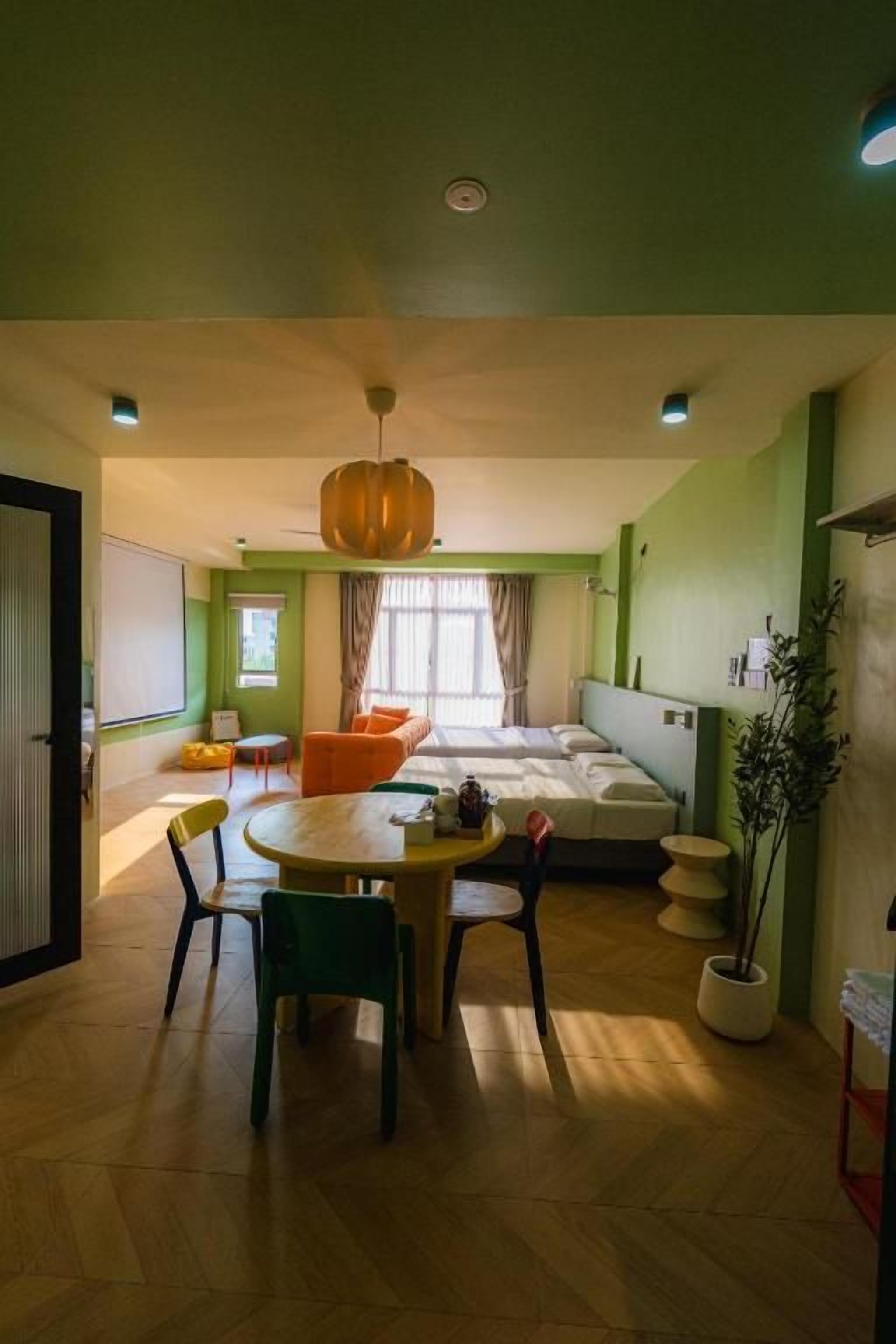 A room with a bed, a dining table with chairs, a hanging light fixture, and a potted plant.