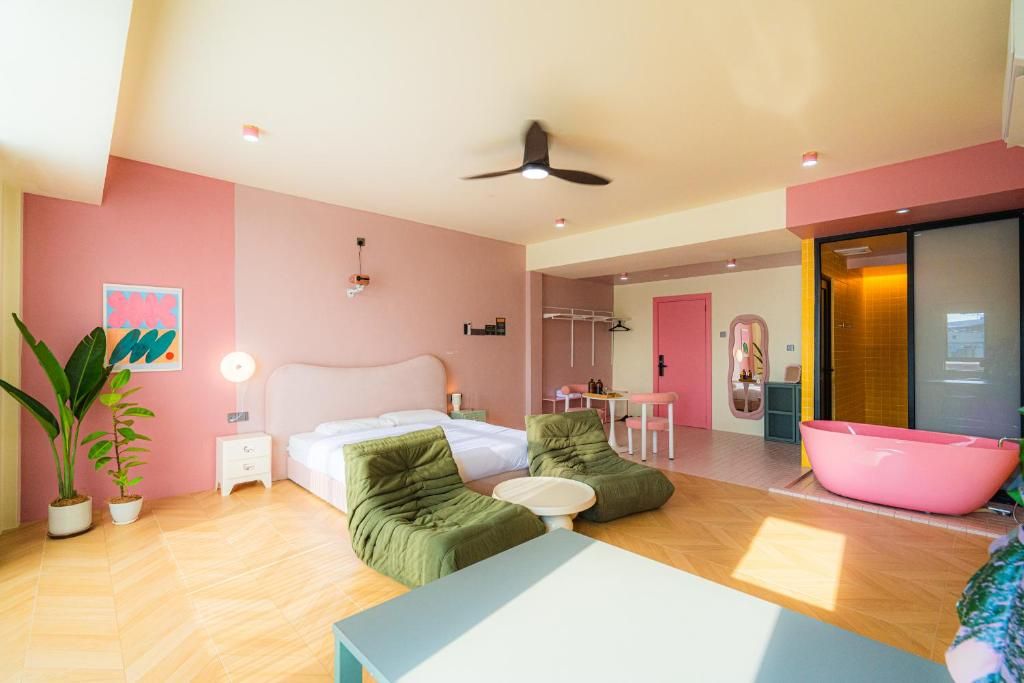A modern bedroom with a bed, two green sofas, a small table, and a pink bathtub.