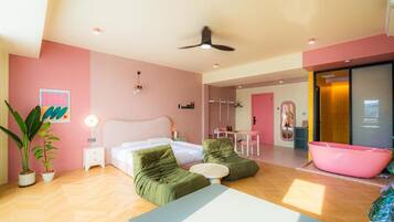 A modern bedroom with a bed, two green sofas, a small table, and a pink bathtub.
