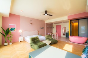 A modern bedroom with a bed, two green sofas, a small table, and a pink bathtub. - Lot 78 (Malacca City)