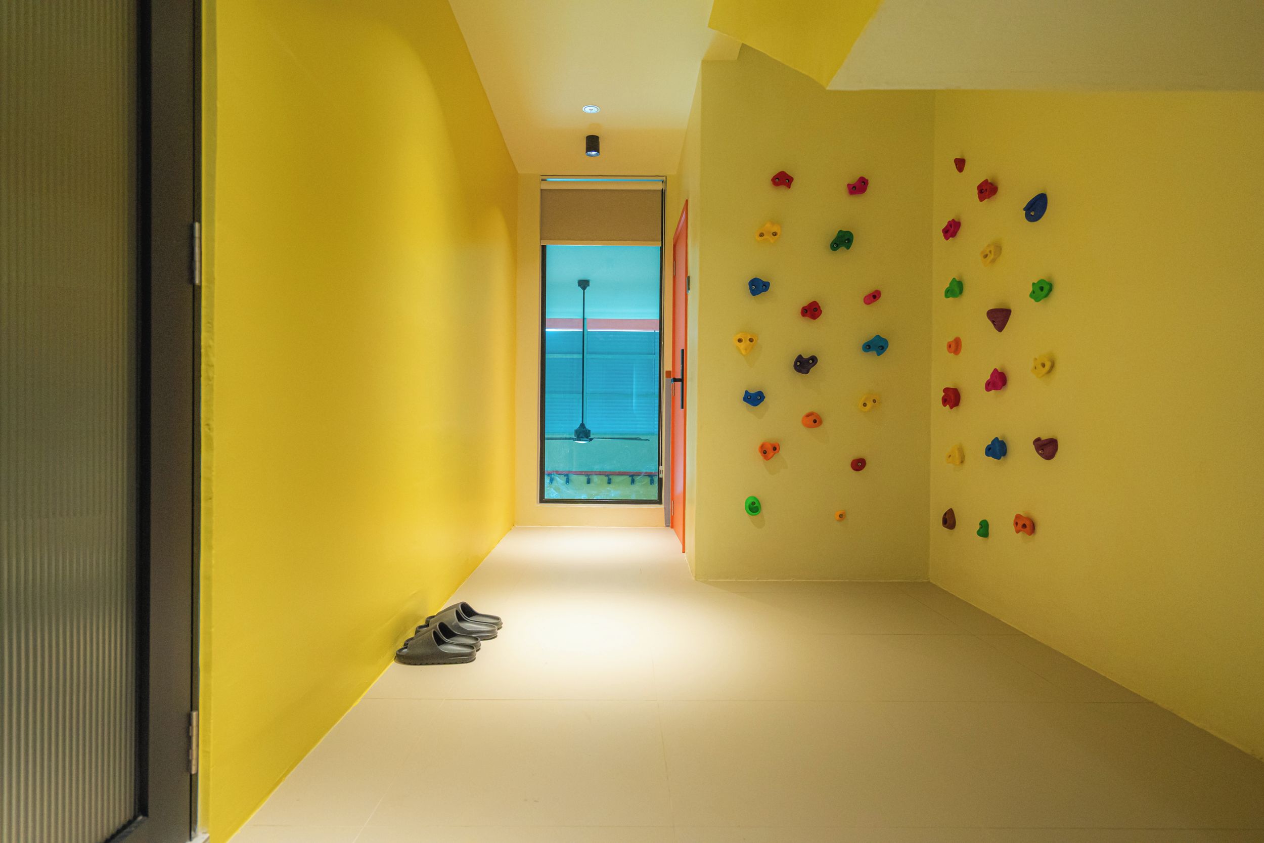 A hallway with a climbing wall on the right, a door on the left, and a pair of shoes on the floor.