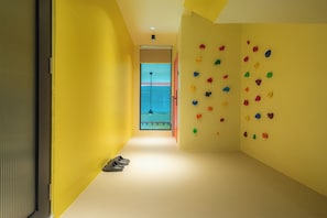 A hallway with a climbing wall on the right, a door on the left, and a pair of shoes on the floor. - Lot 78 (Malacca City)