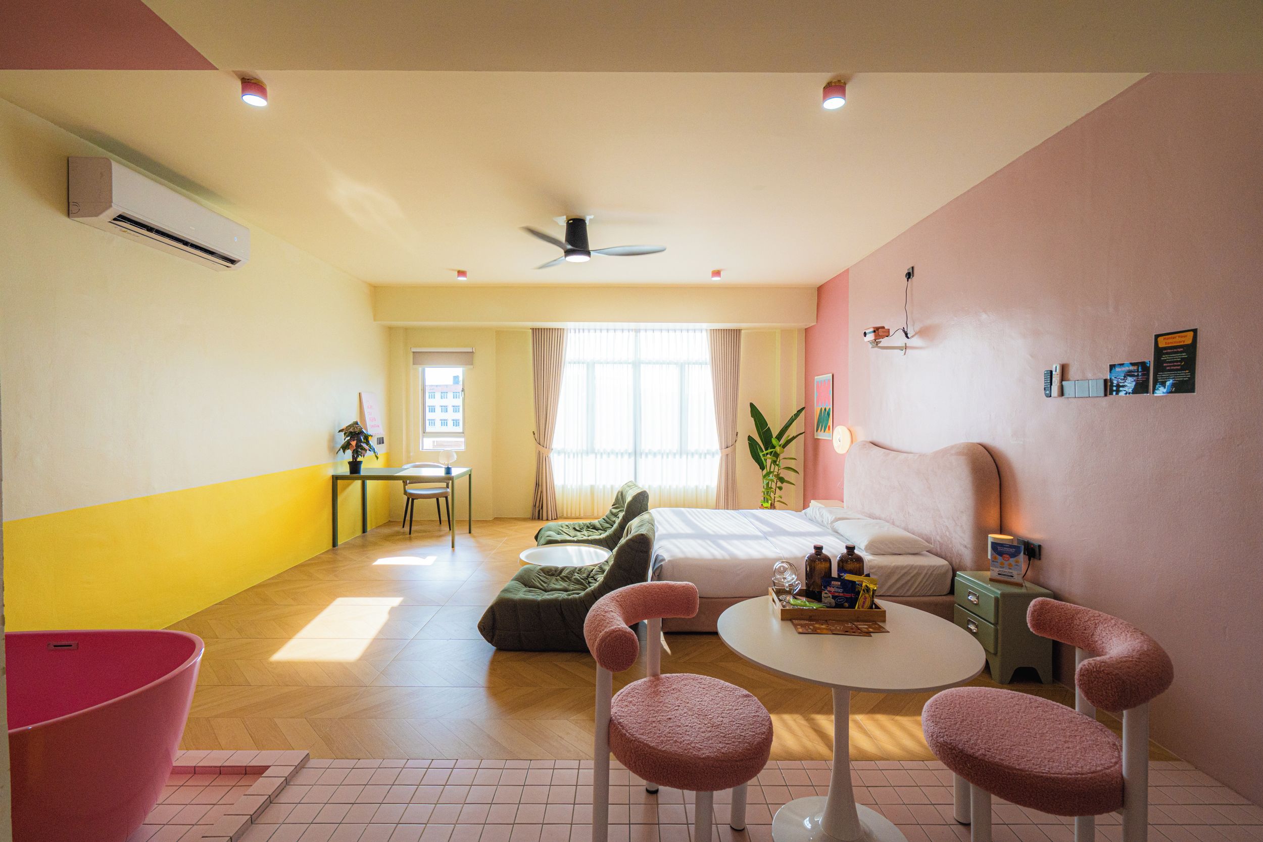 A hotel room with a bed, a desk, a chair, a table, and a plant.