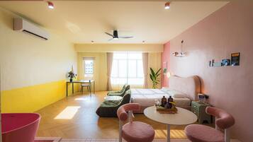 A hotel room with a bed, a desk, a chair, a table, and a plant.