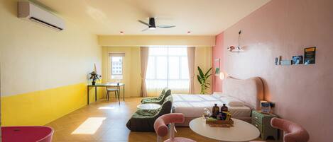 A hotel room with a bed, a desk, a chair, a table, and a plant.