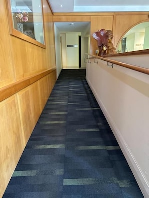 A corridor with a patterned carpet, wooden paneling, and a handrail. - Nan Tien Temple Pilgrim Lodge (Berkeley)