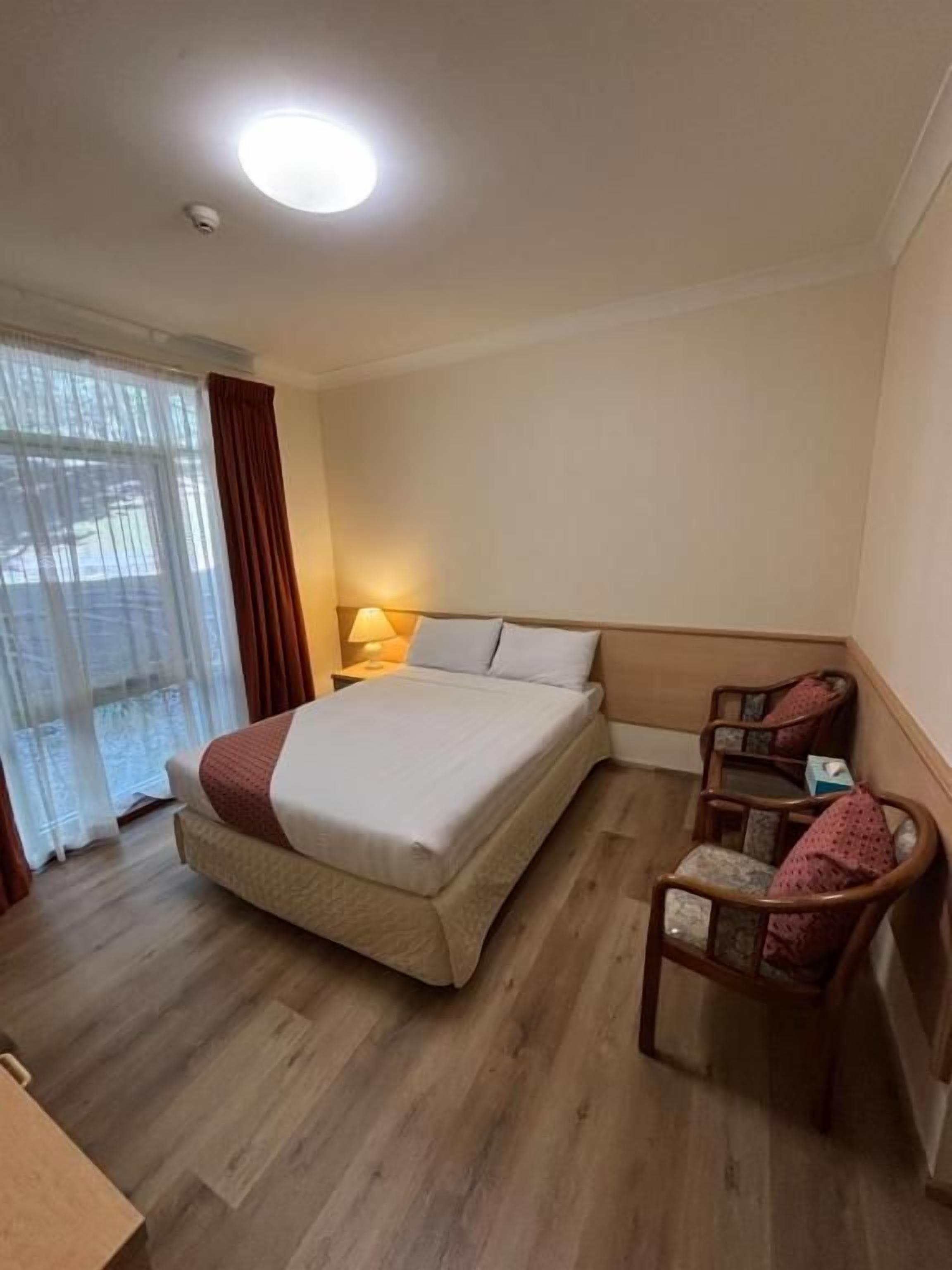 Hotellihuone, jossa on sänky, tuoli, työpöytä ja ikkuna, jossa on verhot.
