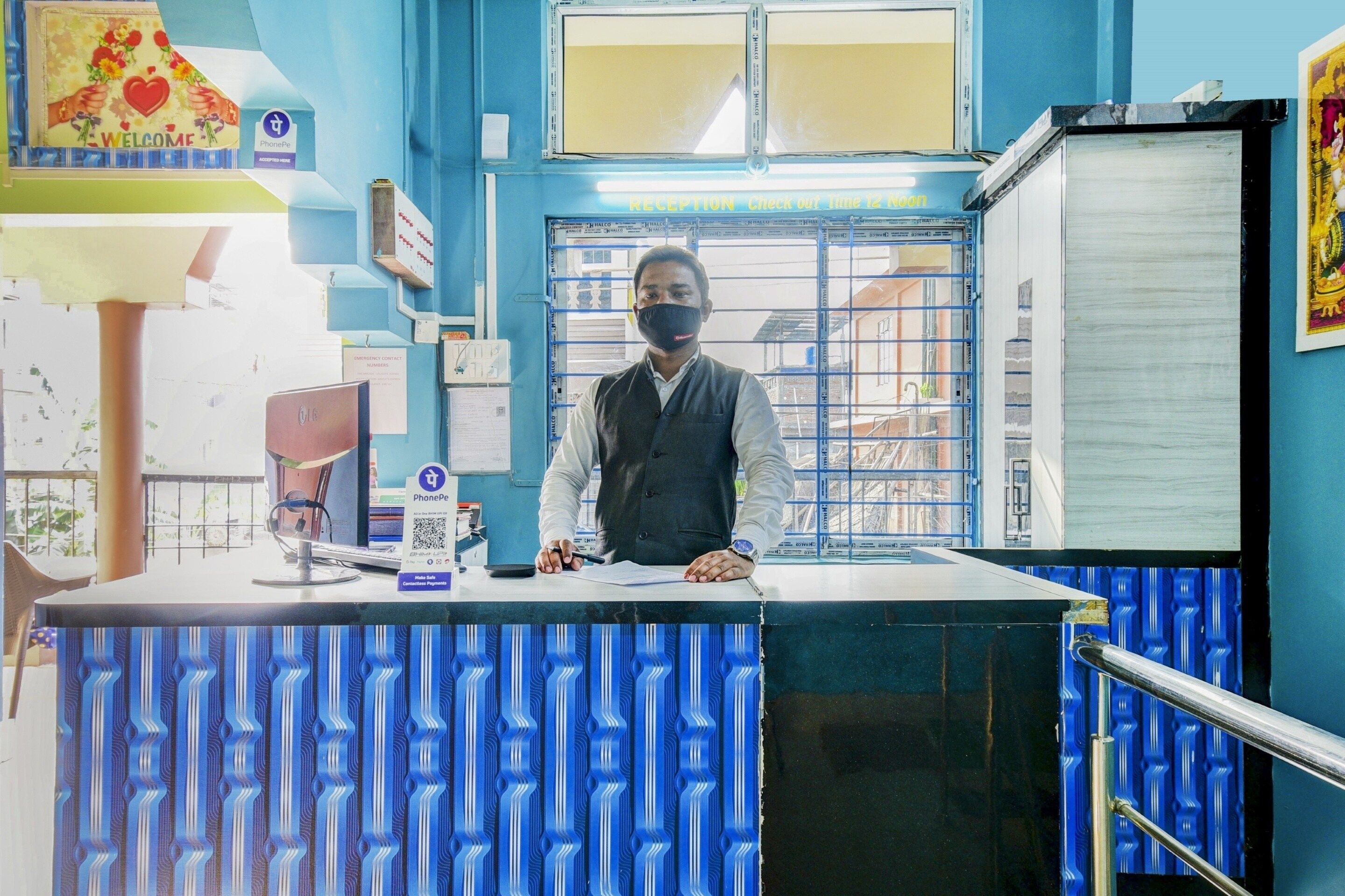 A reception desk with a blue patterned counter, a phone, and a wall-mounted emergency contact number sign.