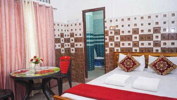 Une chambre d’hôtel avec un lit, une table ornée d’un vase de fleurs, une chaise et une salle de bain visible à travers une porte ouverte.