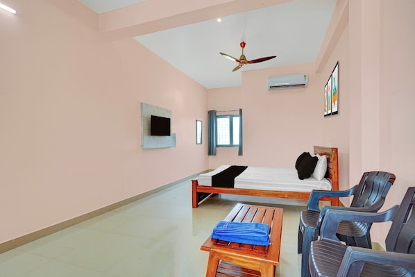 A hotel room with a bed, a desk, chairs, a ceiling fan, an air conditioning unit, and a window. - HOTEL O KSR GRAND (Chittoor)