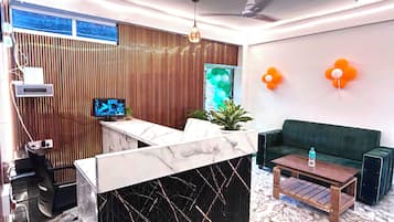 A modern living room with a marble reception desk, a green sofa, a wooden coffee table, and a ceiling fan.