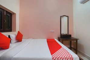 Un dormitorio con cama, almohadas, una mesita de noche, un espejo y un corredor con estampado rojo y blanco.