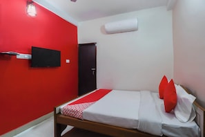 A small, single-bed room with a red wall, a mounted TV, and a white air conditioning unit.