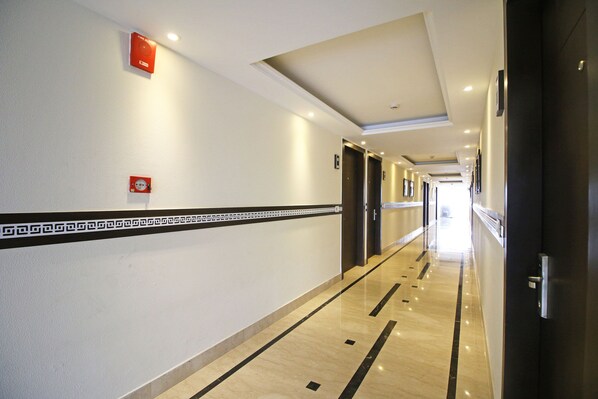 A hotel corridor with a marble floor, a fire alarm on the wall, and doors leading to rooms. - Hotel O Central Palace (Dehradun)