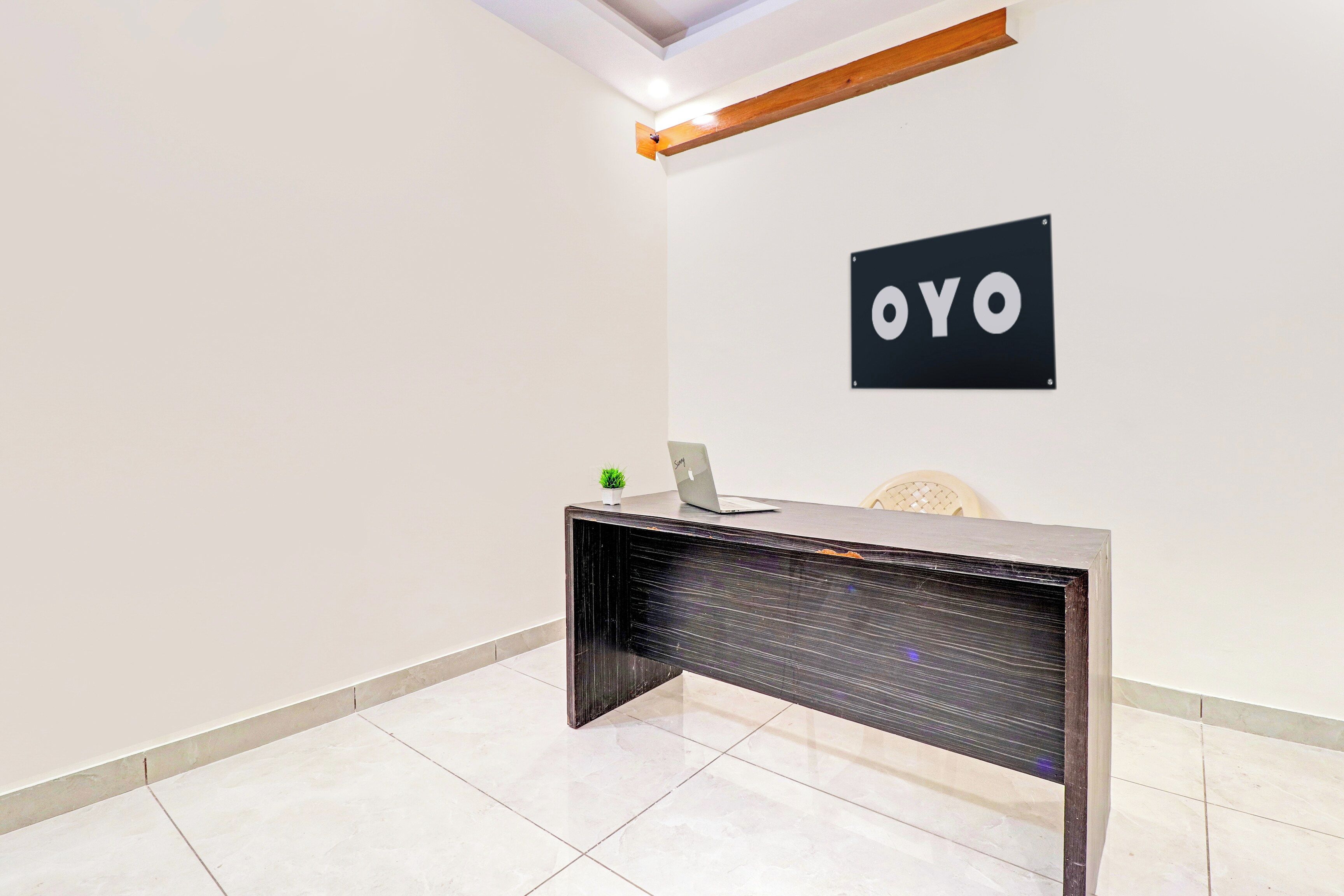 Ein moderner Empfangstresen mit einem Laptop, einer kleinen Topfpflanze und einem Schild mit der Aufschrift 'OYO'.