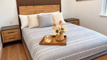 A bedroom with a wooden bed frame, a headboard with a vertical panel design, and a bedside table with a drawer.