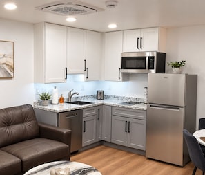 Cozinha moderna com eletrodomésticos de aço inoxidável, bancada de mármore e armários cinzentos.