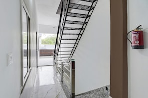 A corridor with a metal rack, a fire extinguisher, and a door leading to an outdoor area. - HOTEL O VIP HILL HOMESTAY (Dehradun)