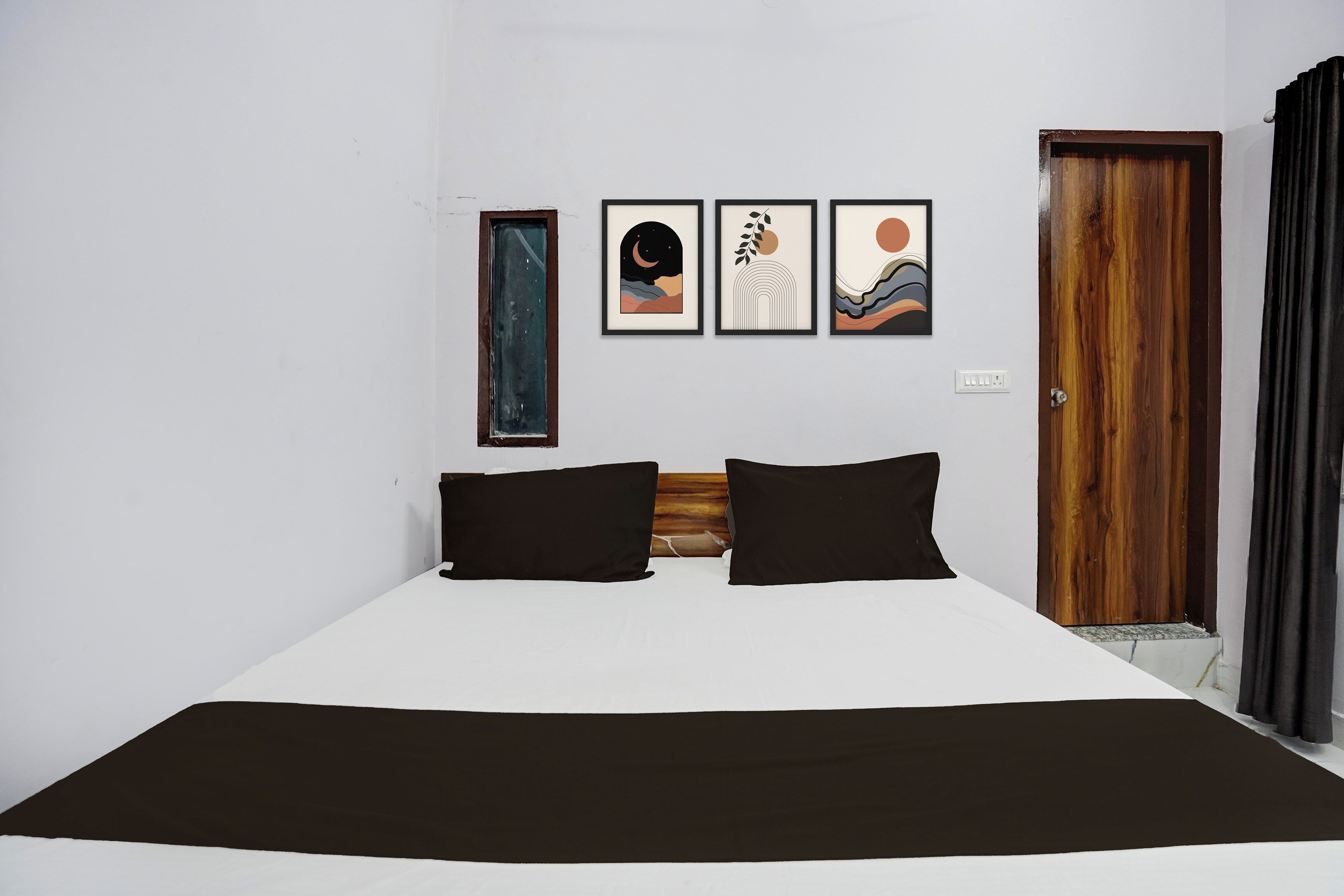 Un dormitorio con una cama, dos almohadas negras, un cabecero de madera, una puerta y tres cuadros en la pared.