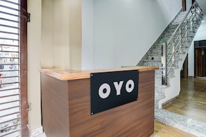 A reception desk with a sign that reads 'OYO' in a modern building with a staircase. - HOTEL O VIP HILL HOMESTAY (Dehradun)