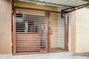 A metal gate with horizontal bars and a central handle, leading to a building with a beige exterior wall. - HOTEL O VIP HILL HOMESTAY (Dehradun)