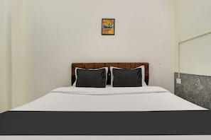 A single bed with a wooden headboard, two pillows, and a white bedspread. - Hotel O by OYO Second Home Residency (Dehradun)