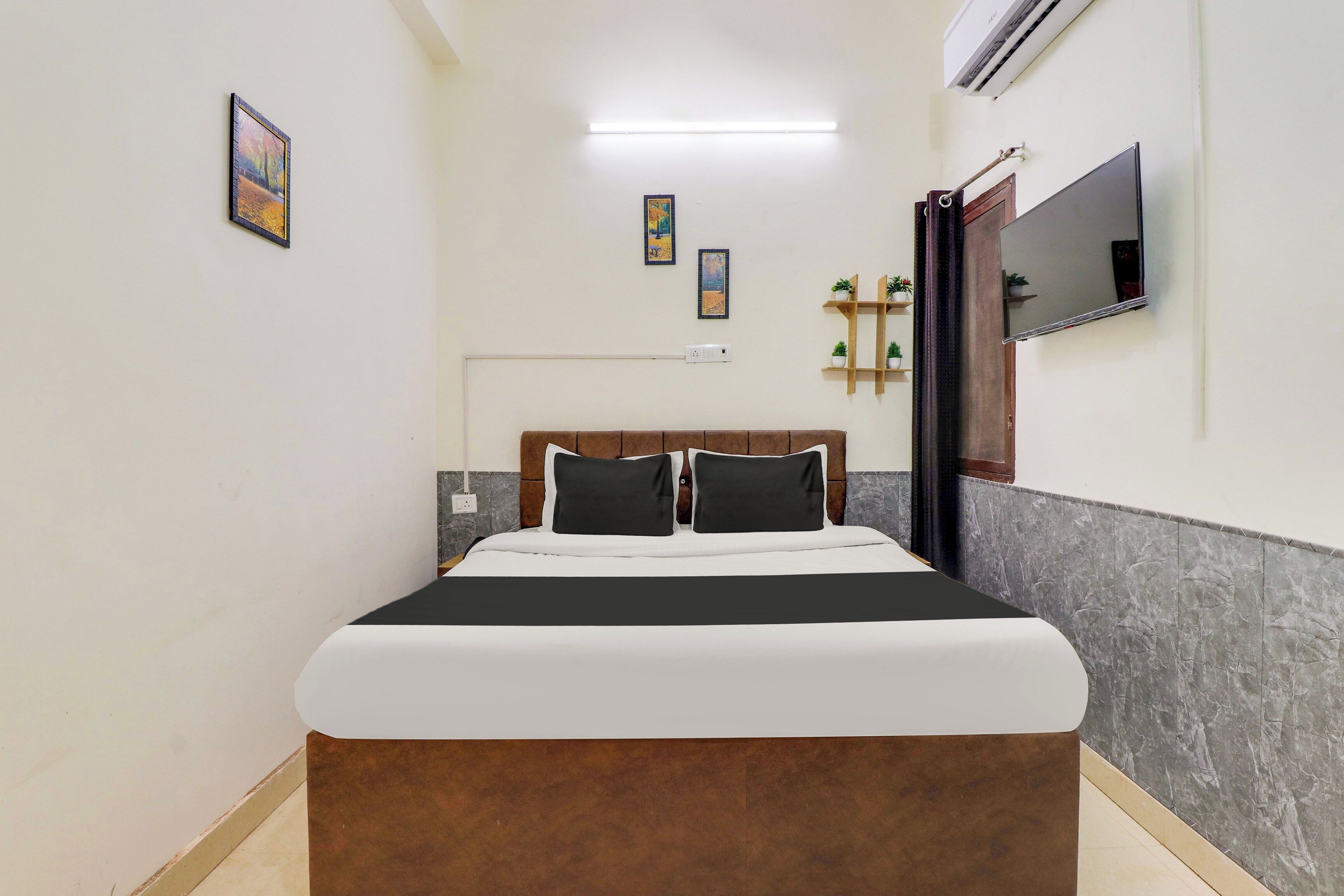 A bedroom with a bed, a wall-mounted TV, and a ceiling light.