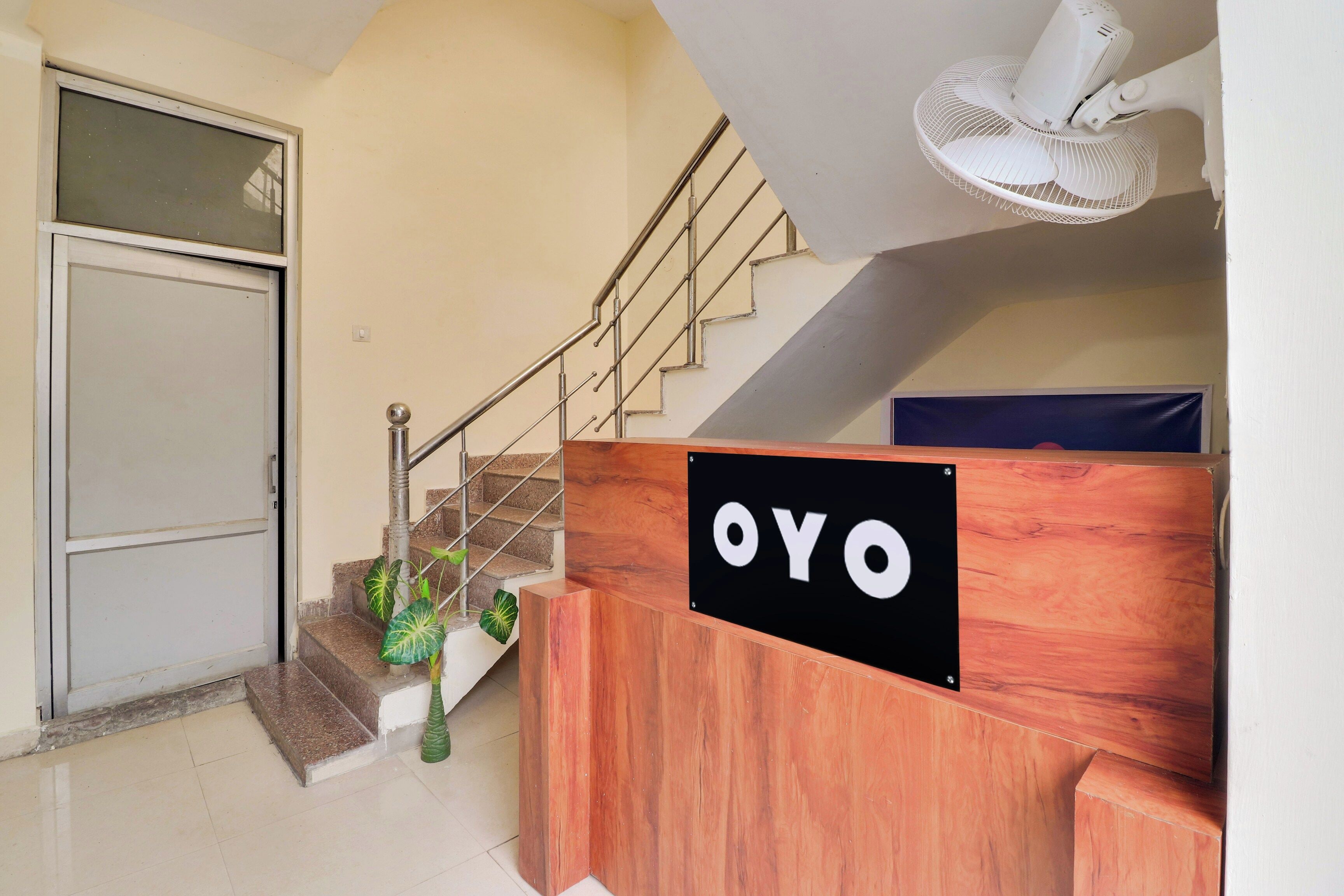 A reception desk with a sign that reads 'OYO' in a hotel lobby with a staircase and a door.