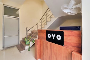 A reception desk with a sign that reads 'OYO' in a hotel lobby with a staircase and a door. - Hotel O by OYO Second Home Residency (Dehradun)