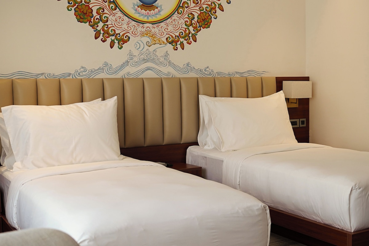 A hotel room with two beds, a decorative wall mural, and a nightstand with a lamp.