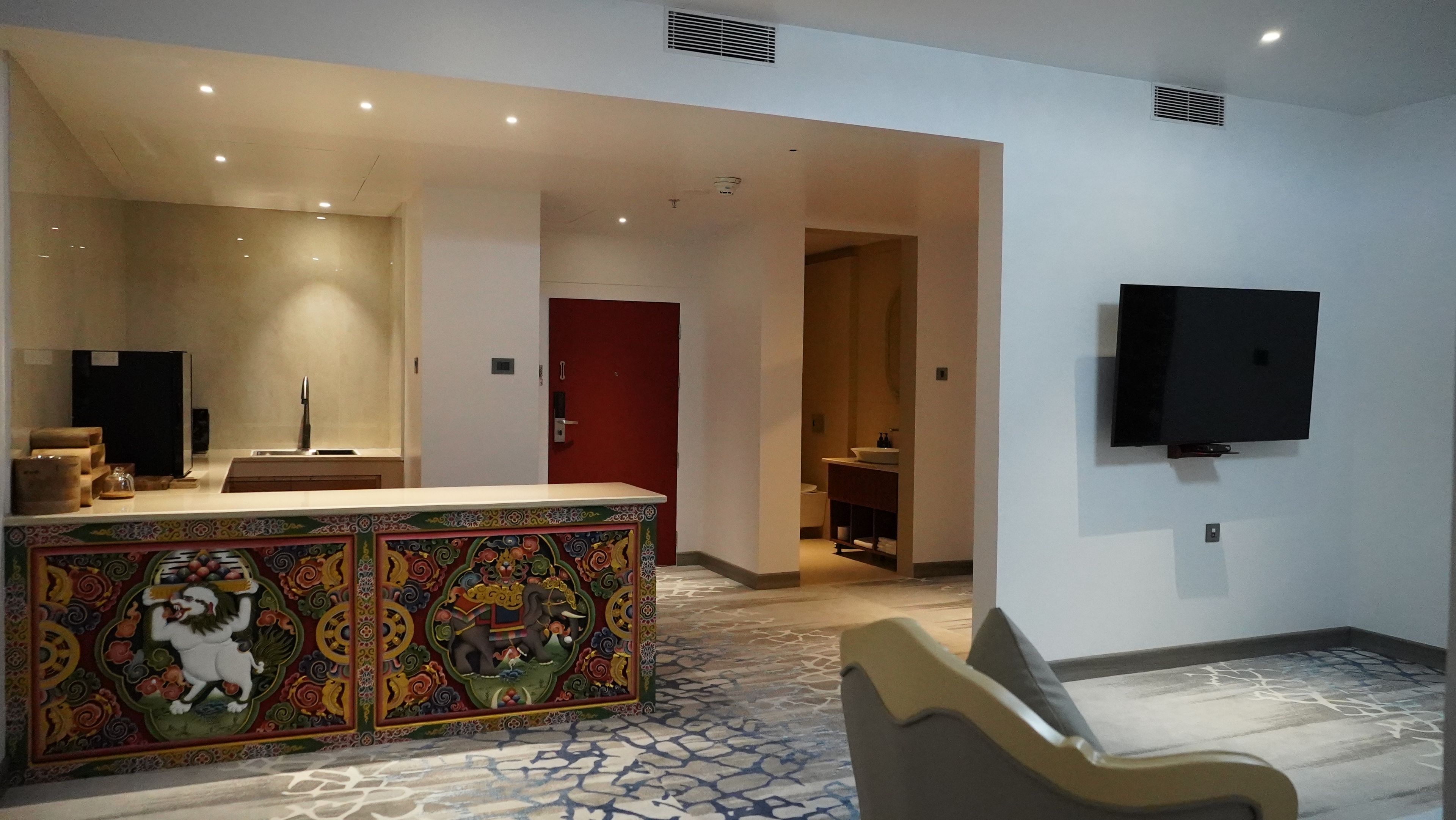 A hotel lobby with a reception desk, a television mounted on the wall, and a patterned carpet.