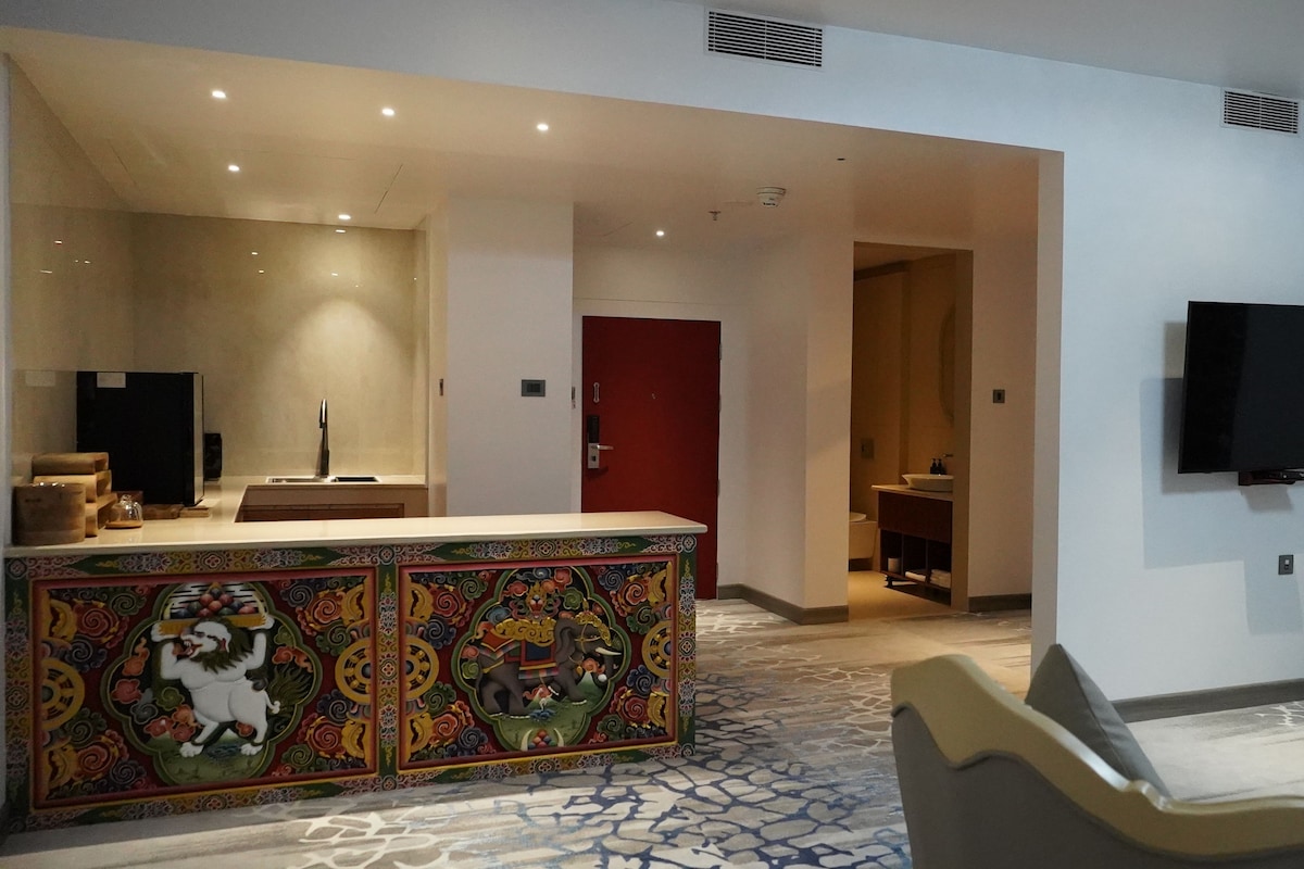 A hotel lobby with a reception desk, a television mounted on the wall, and a patterned carpet.
