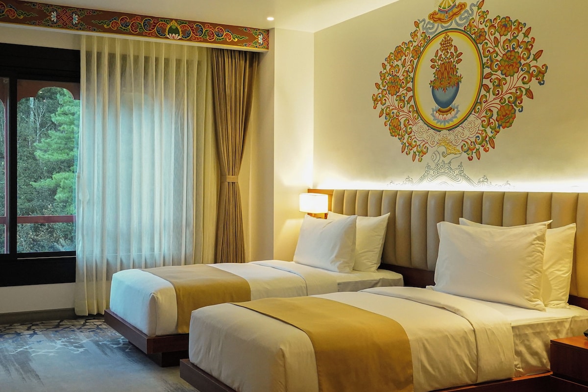 A hotel room with two beds, a large window with curtains, and a decorative wall piece.