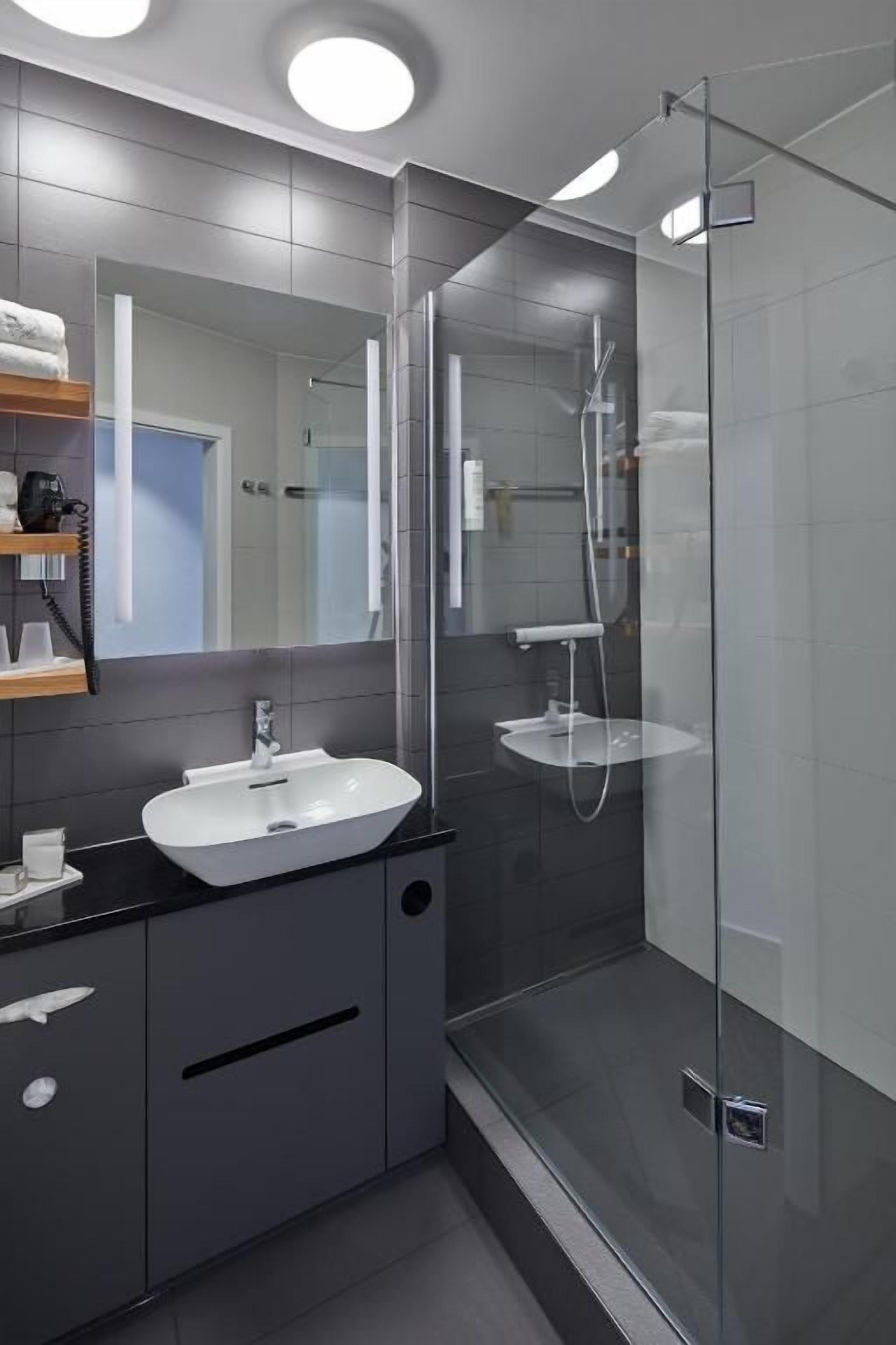 Un baño moderno con cabina de ducha de vidrio, un lavabo blanco y un espejo sobre el lavabo.
