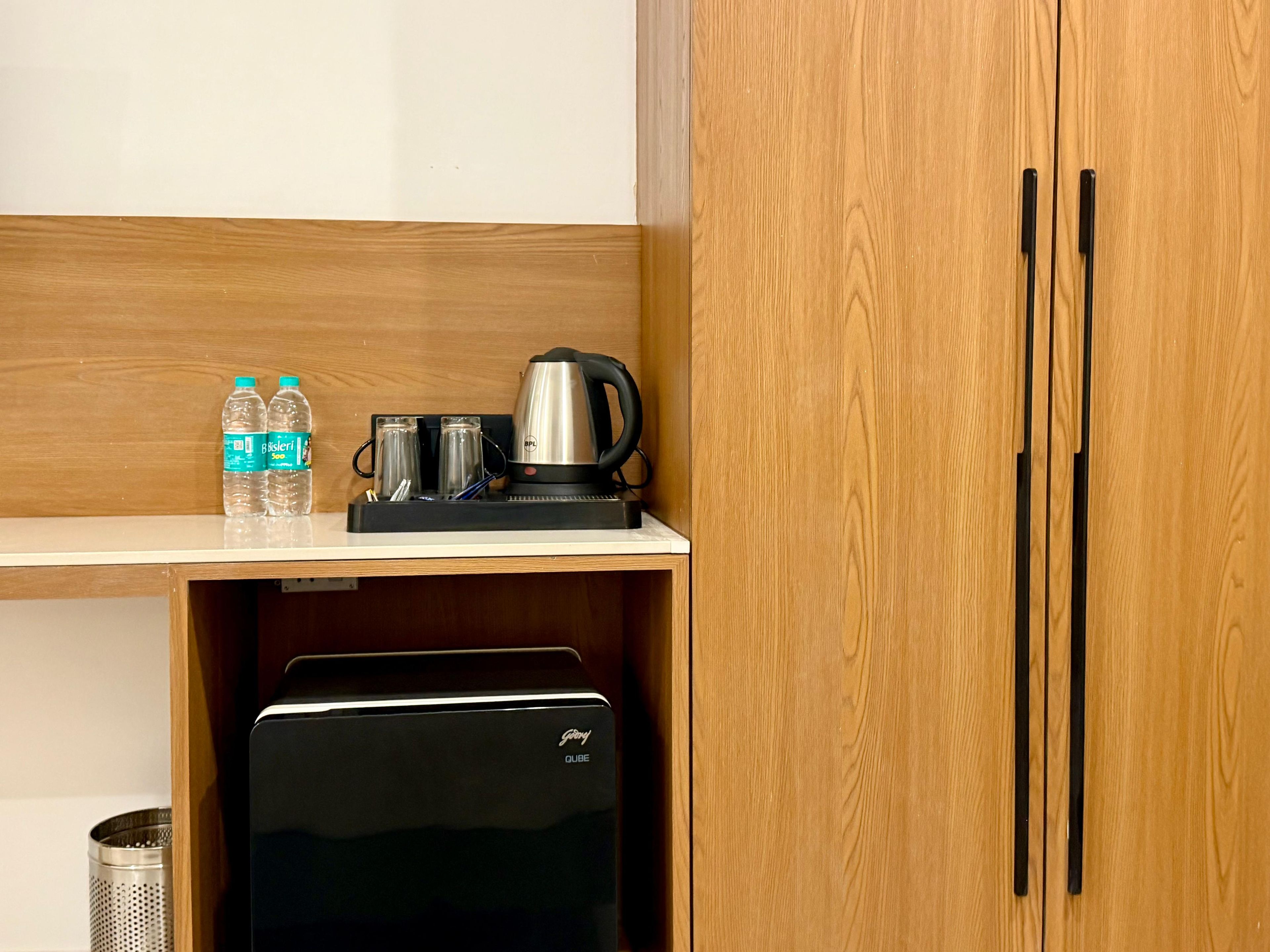 Una kitchenette con cafetera, dos botellas de agua y un refrigerador pequeño.