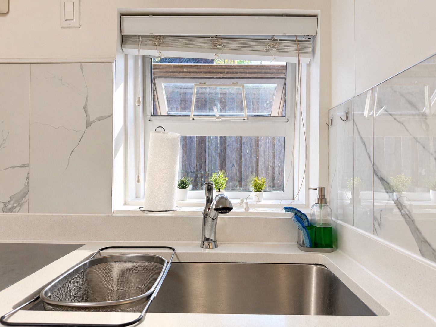 A kitchen with a stainless steel sink, a window with a view of the outside, and a small potted plant on the windowsill.