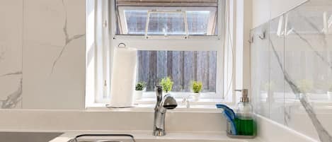 A kitchen with a stainless steel sink, a window with a view of the outside, and a small potted plant on the windowsill.