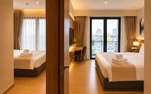 Camera d'albergo con due letti, una scrivania, una sedia e vista sulla città attraverso ampie finestre.