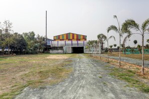 Un espacio abierto con un edificio al fondo, un sendero de tierra que lo conduce y vegetación escasa.