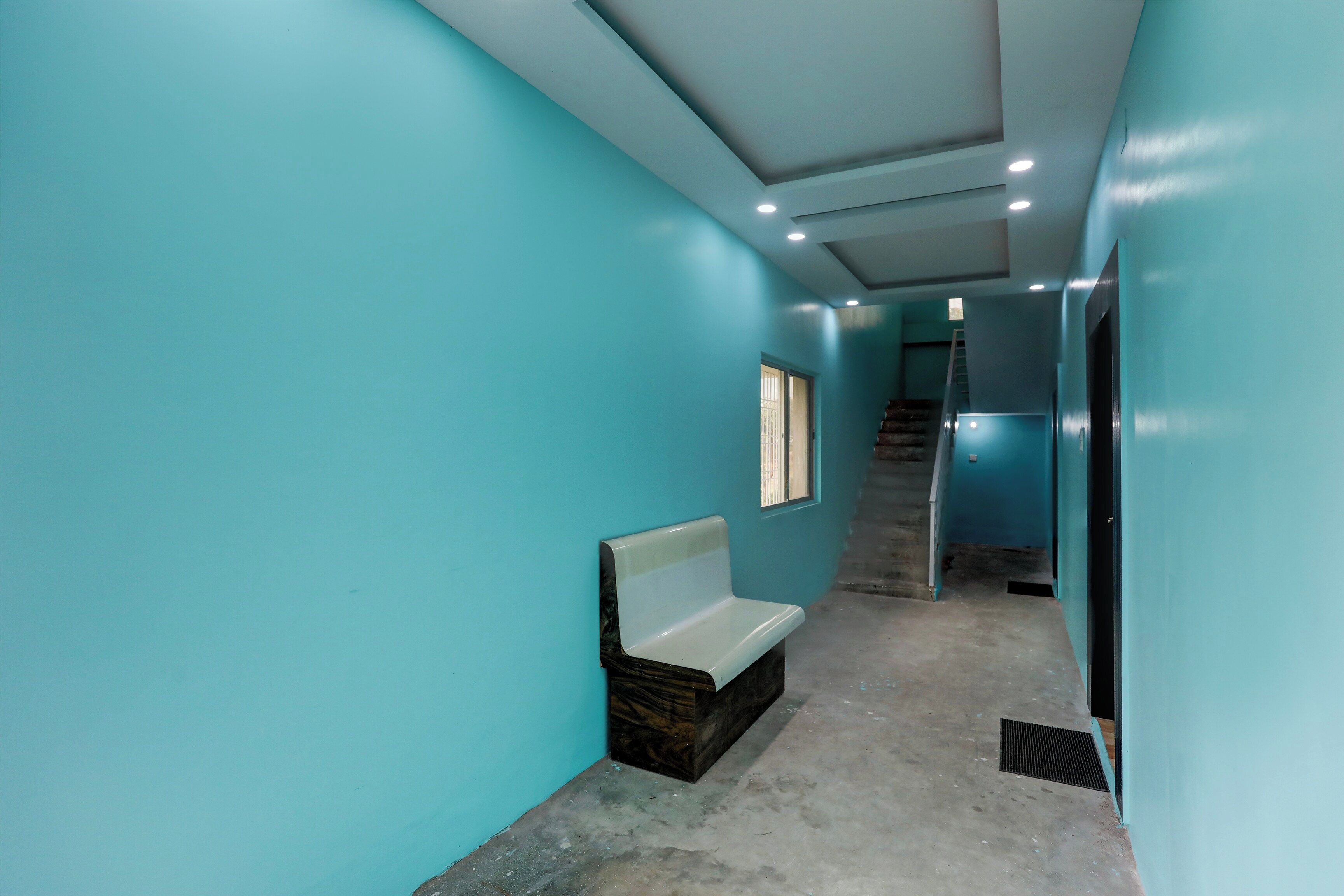 A hallway with teal walls, a bench, and a staircase leading to another level.